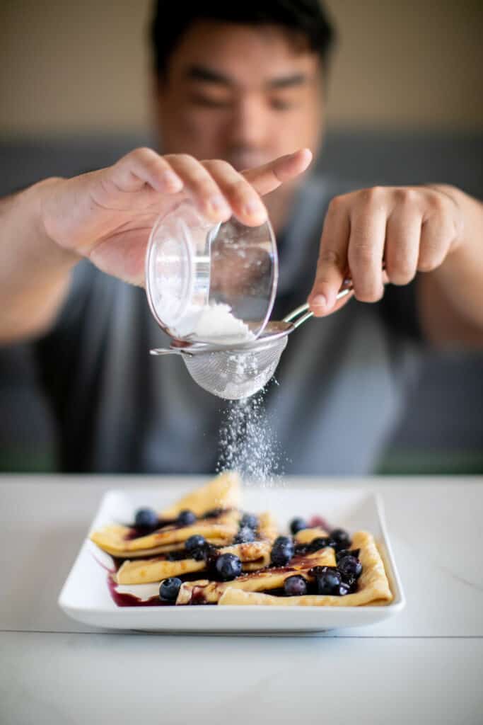 Man dusting the french crepes with powdered sugar