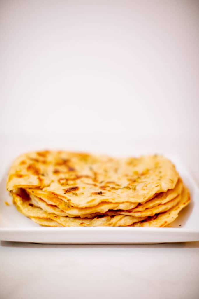 Indian naan bread prepared on a white plate placed on a white surface