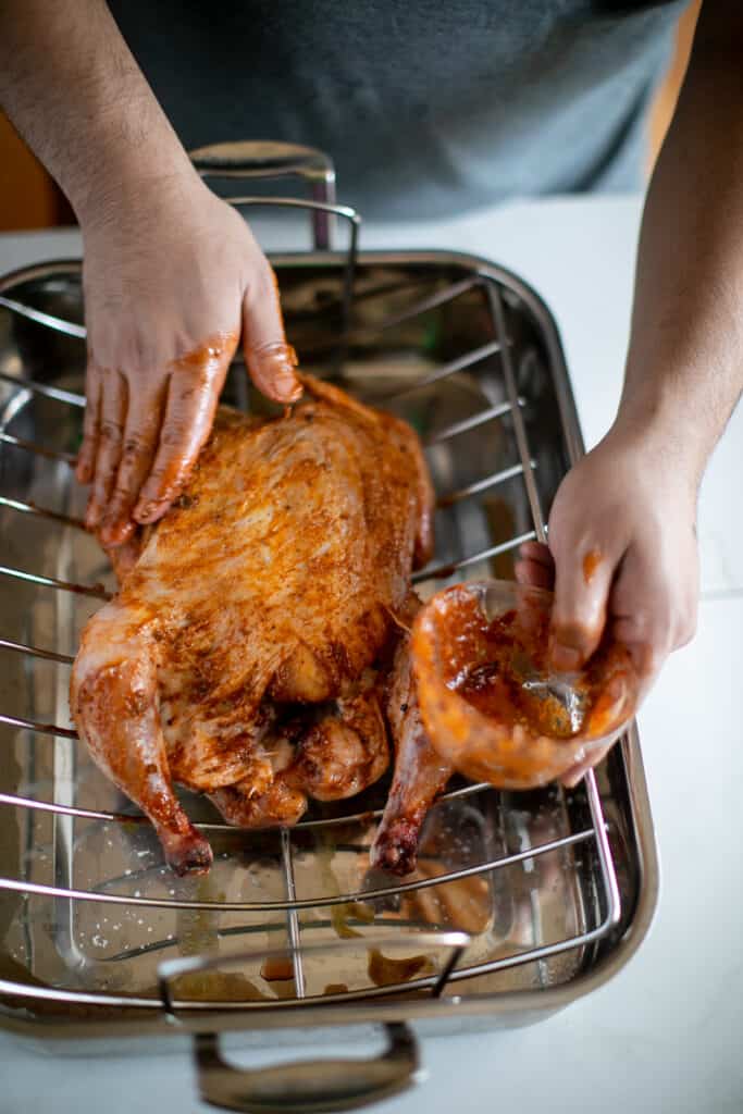 Raw whole chicken being filled with spices before baking