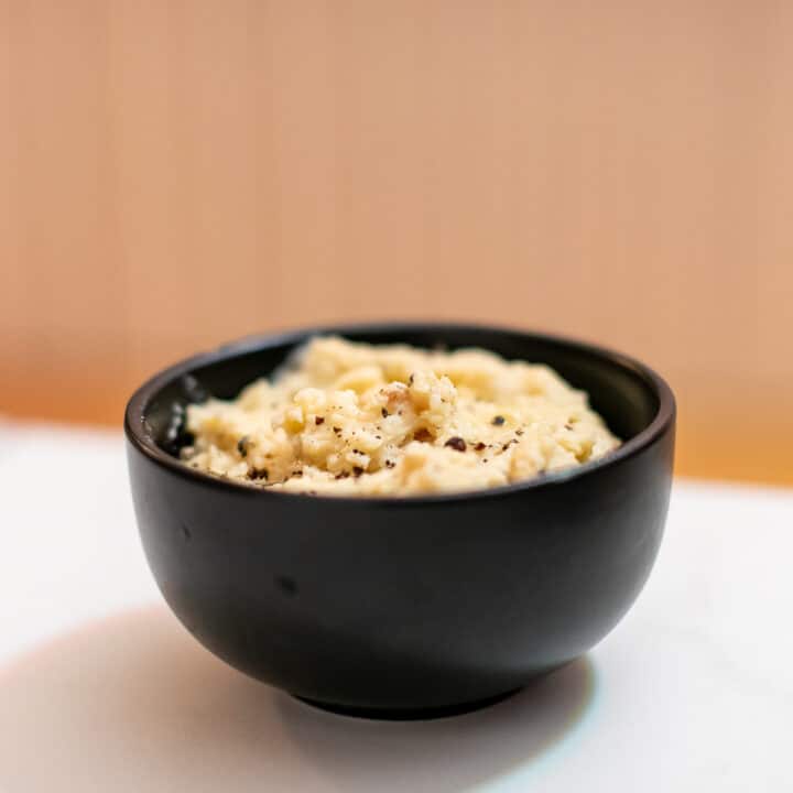 Garlic mashed potato served in a black bowl placed on a white surface
