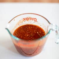 Marinara sauce mixed with herbs was placed in a pyrex measuring cup on a white surface