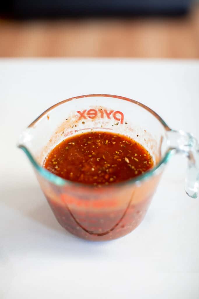 Marinara sauce mixed with herbs was placed in a pyrex measuring cup on a white surface