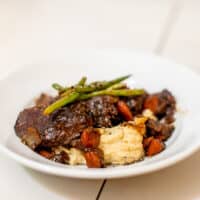 Stovetop pot roast meat paired with mashed potatoes topped with string beans served on a white bowl placed on a white surface