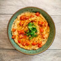 A top view of vegan baba ganoush garnished with tomatoes and herbs served in a green bowl