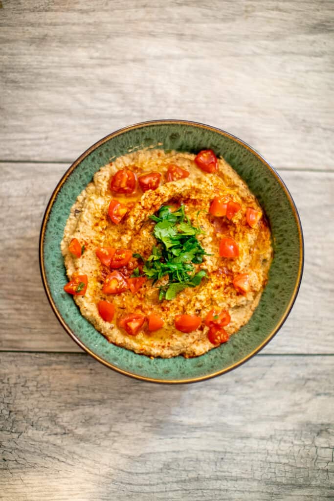 A top view of vegan baba ganoush garnished with tomatoes and herbs served in a green bowl