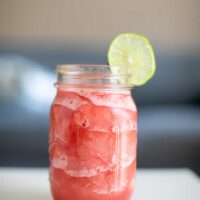 Watermelon daiquiri with a slice of lime served in a mason jar placed on a white table