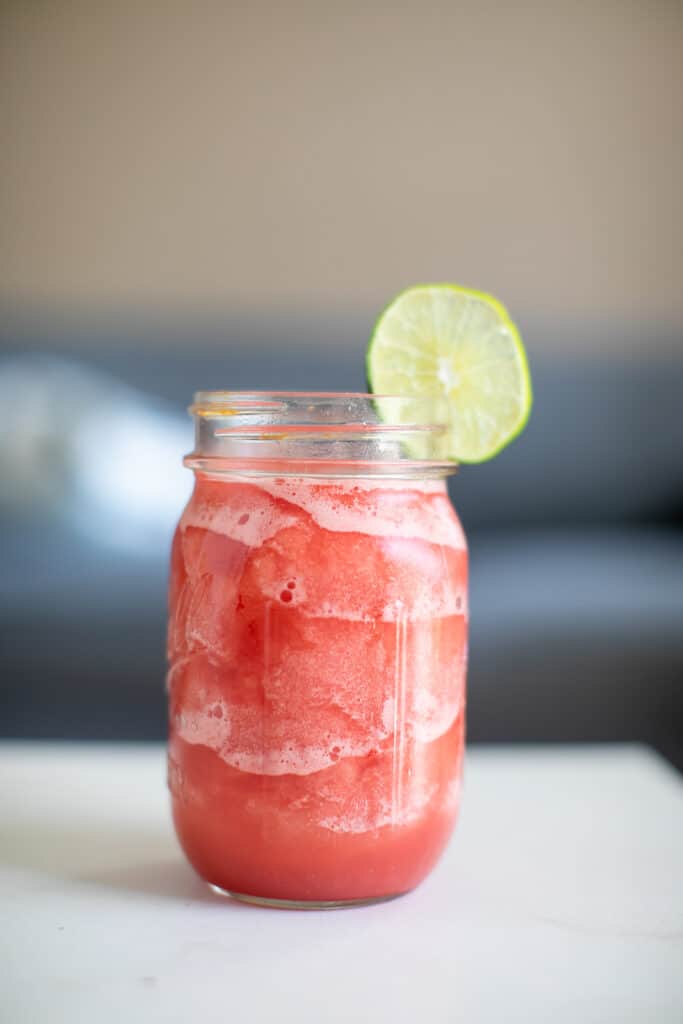 Watermelon daiquiri with a slice of lime served in a mason jar placed on a white table