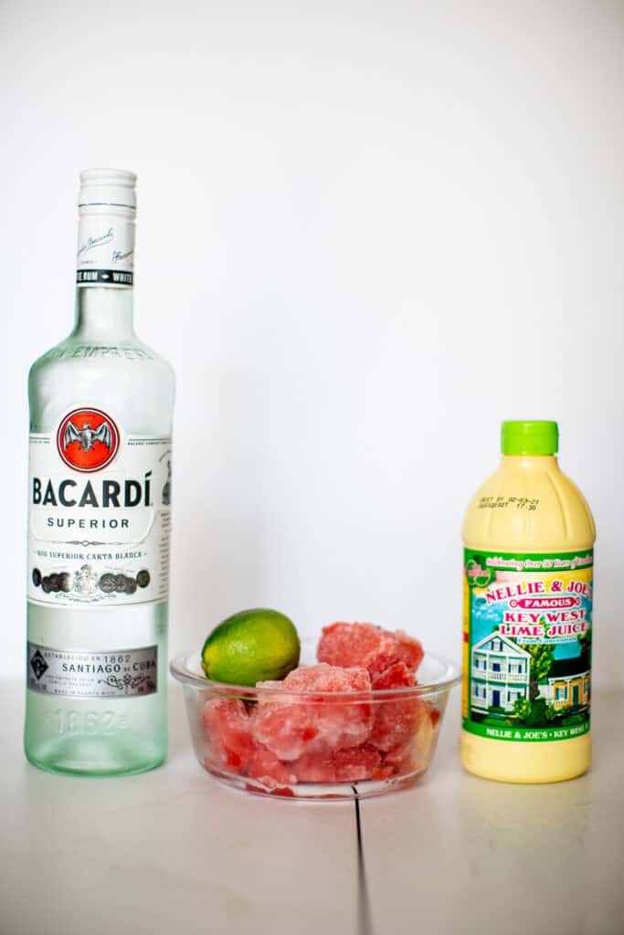 Bottle of Bacardi. bottle of key lime juice and frozen watermelon placed in a table