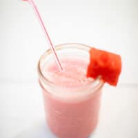 A top view of a watermelon smoothie with yogurt and a slice of watermelon in a mason jar placed on a white table