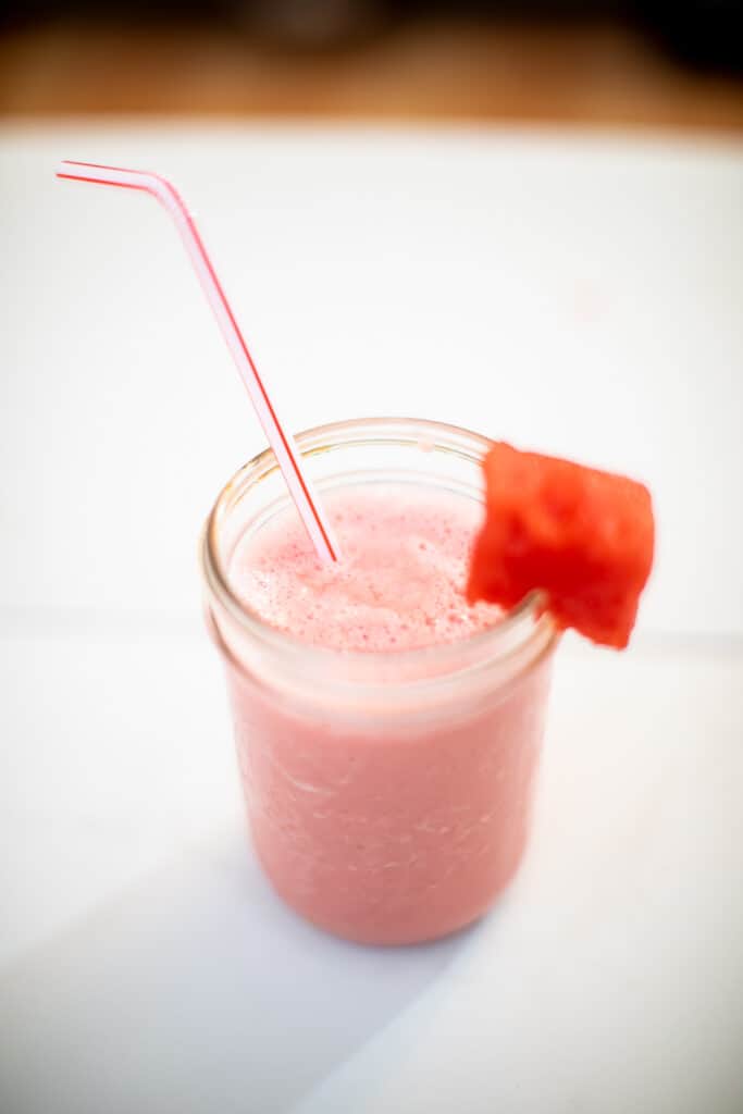 A top view of a watermelon smoothie with yogurt and a slice of watermelon in a mason jar placed on a white table