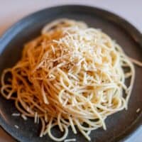 Parmesan buttered noodles with cheese served on a black plate placed on a white surface