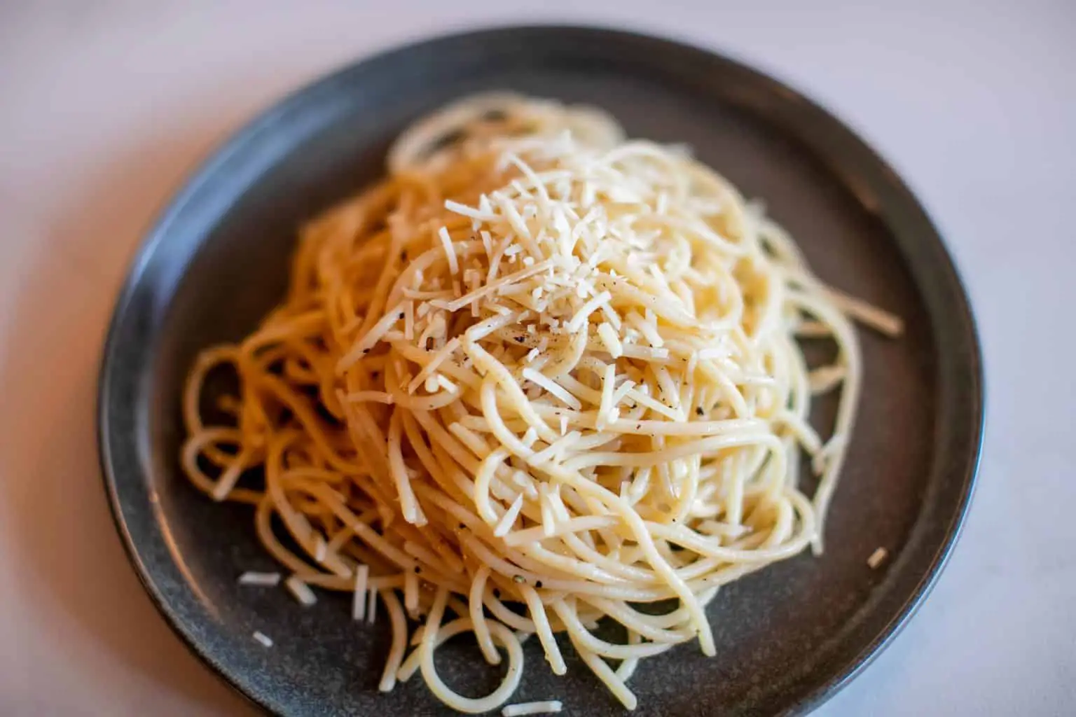 Parmesan buttered noodles with cheese served on a black plate placed on a white surface