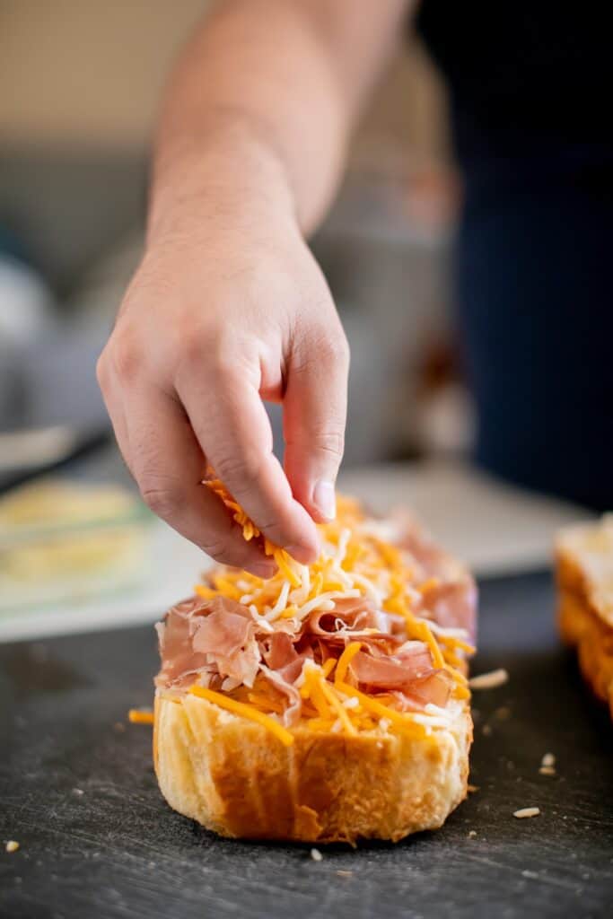 Person putting cheese on top of aged ham on a piece of bread