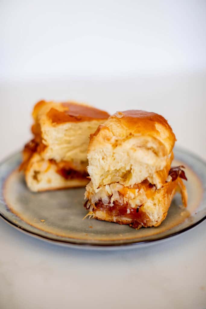 Two pieces of buns filled with oven-baked ham and cheese sliders served on a ceramic plate placed on a white table