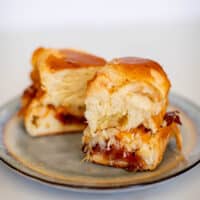 Two pieces of buns filled with oven-baked ham and cheese sliders served on a ceramic plate placed on a white table