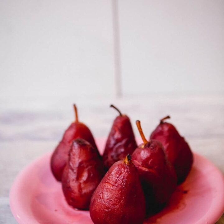Six pieces of poached pears on a white plate placed on a wooden surface
