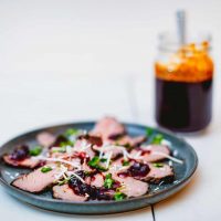 Tri tip with cranberry barbeque sauce and basil served on a blue ceramic plate placed on a white table