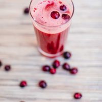 A top view of cranberry juice in a tall glass with fresh cranberries around a wooden surface