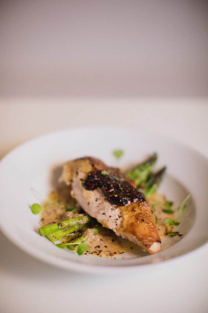 Oven-roasted whole Pheasant with sauce and asparagus served in a white bowl