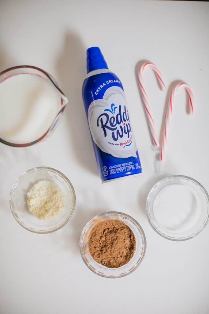 Whipped cream, sugar, cocoa powder, milk and candy cane on the table