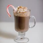 Peppermint hot chocolate with marshmallows and candy cane served in a clear glass mug with a handle