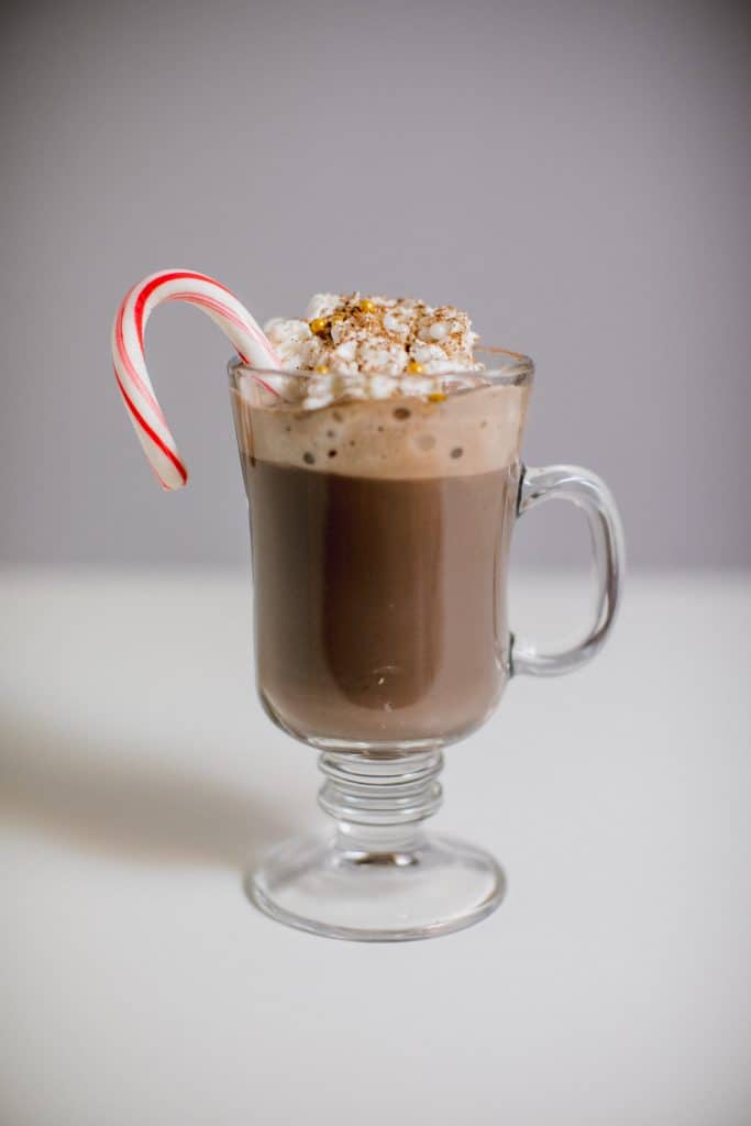 Peppermint hot chocolate with marshmallows and candy cane served in a clear glass mug with a handle