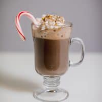 Peppermint hot chocolate with marshmallows and candy cane served in a clear glass mug with a handle