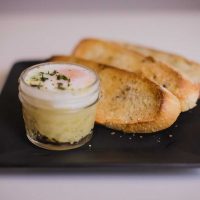 Instant pot copycat eggslut in a small glass container with buttered toast placed on a black plate