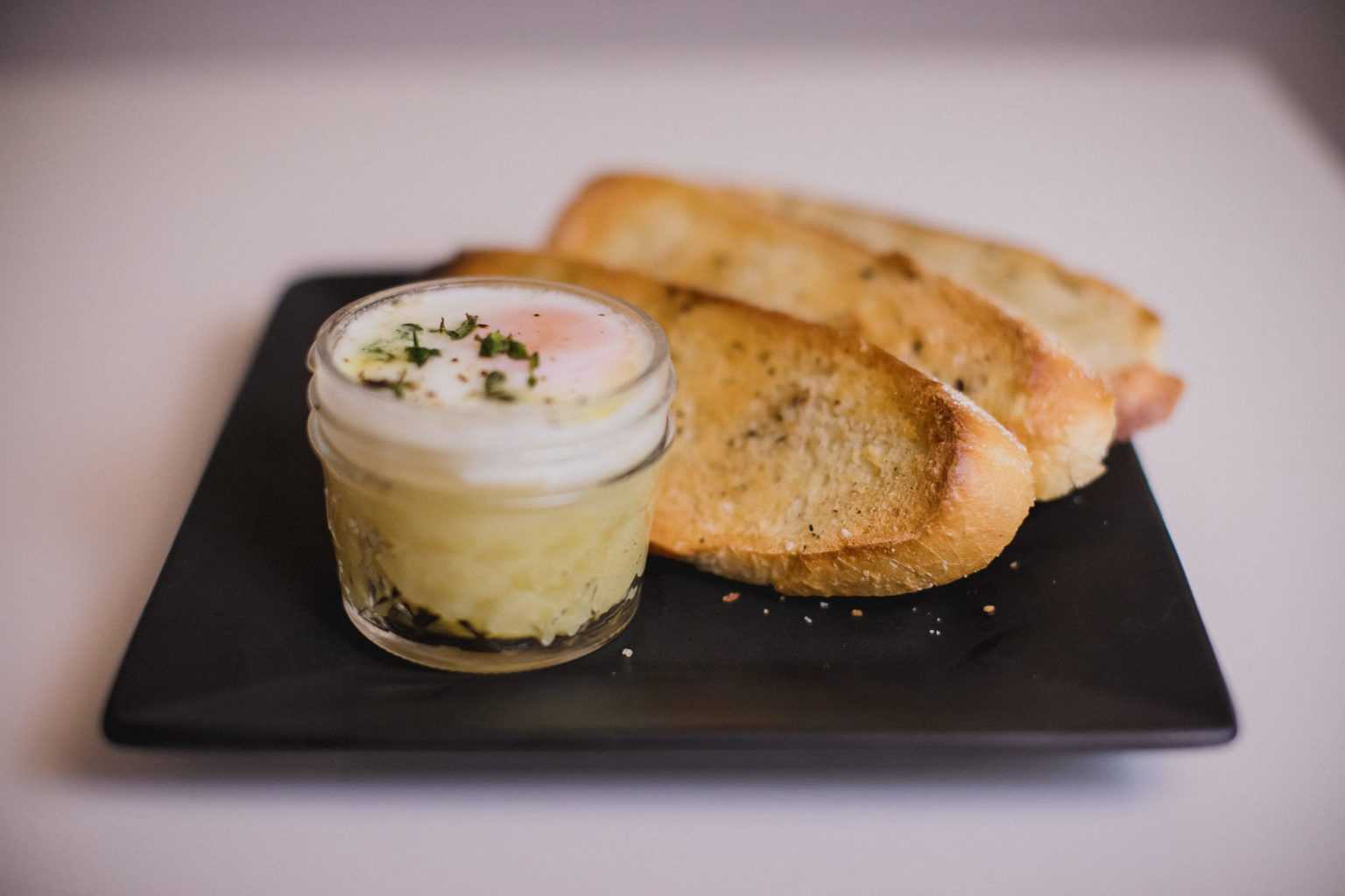 Instant pot copycat eggslut in a small glass container with buttered toast placed on a black plate