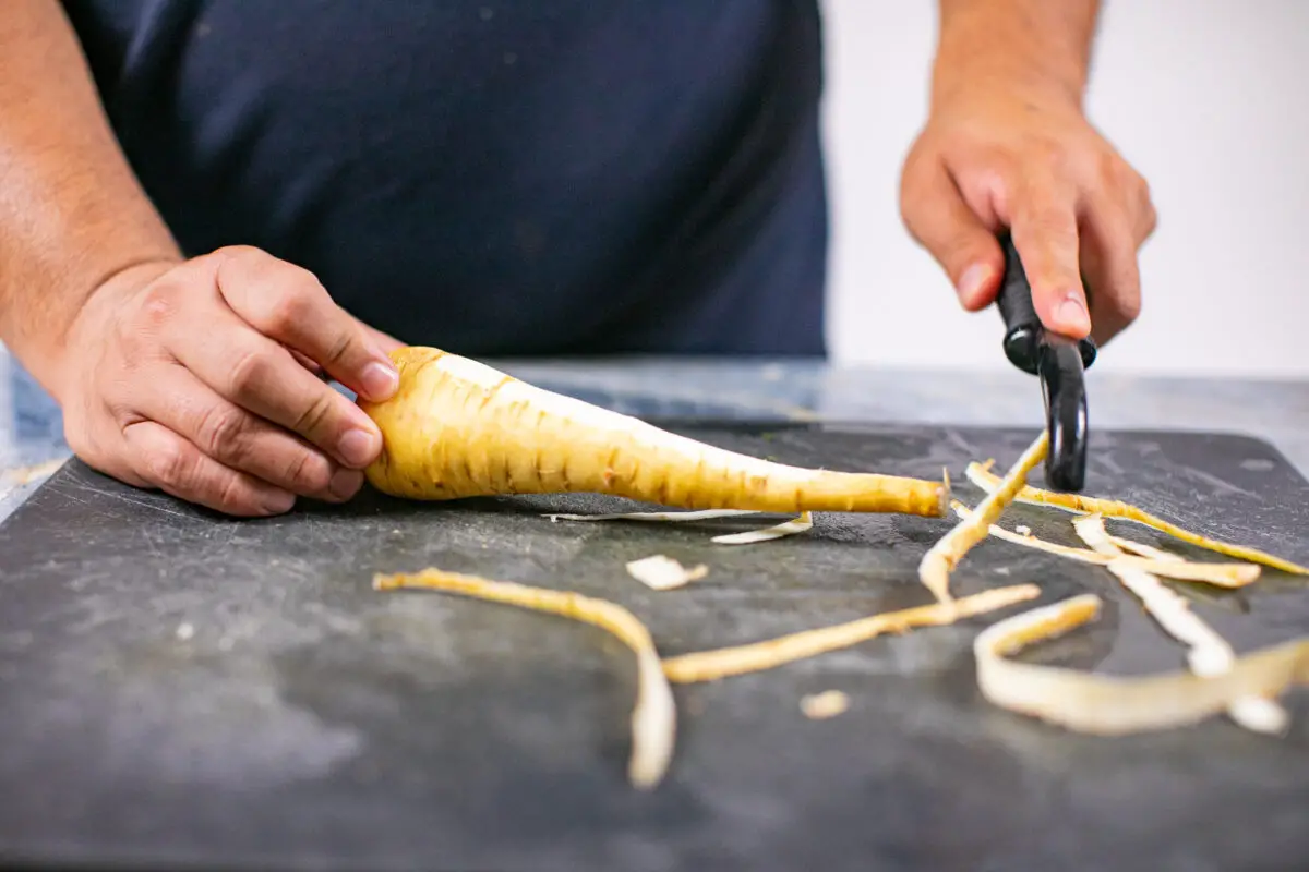 Man peeling parsnips with a peeler on a black cutting board in the kitchen