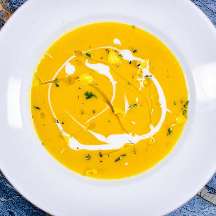 A top view of a butternut squash soup served on a white plate placed on a blue surface