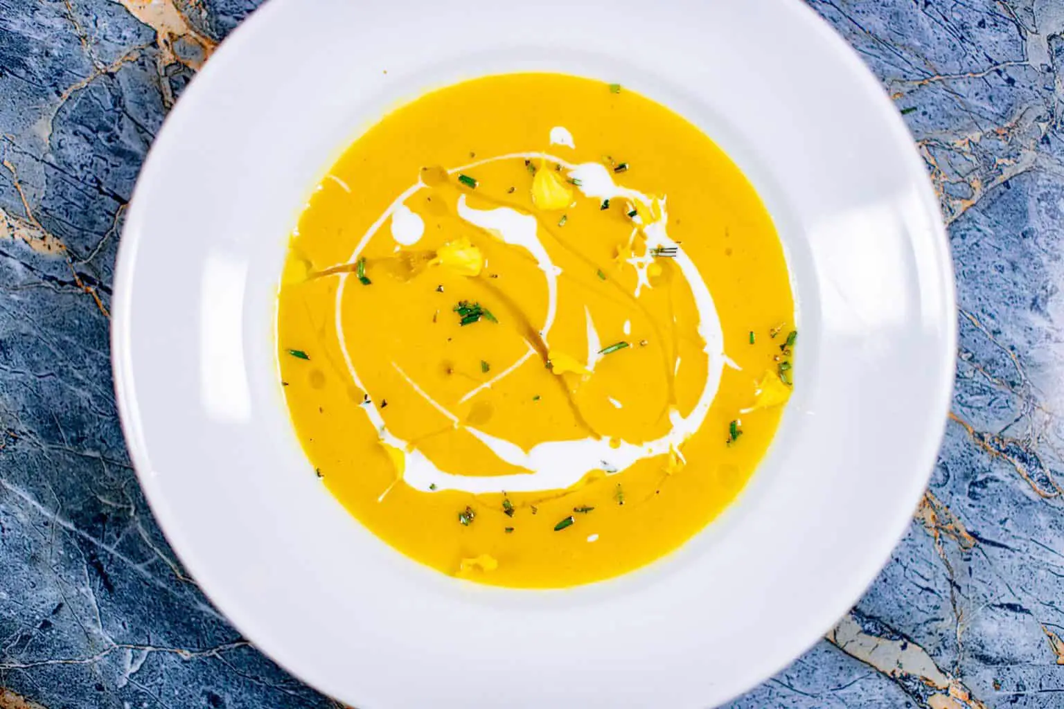 A top view of a butternut squash soup served on a white plate placed on a blue surface