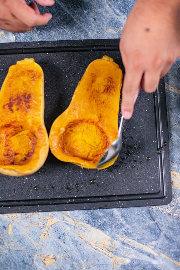 Person scooping out roasted butternut squash from pan