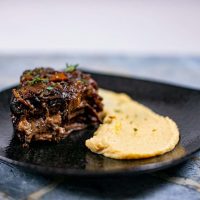 Garlic mashed parsnips with meat garnished with herbs served on a black plate placed on a blue surface