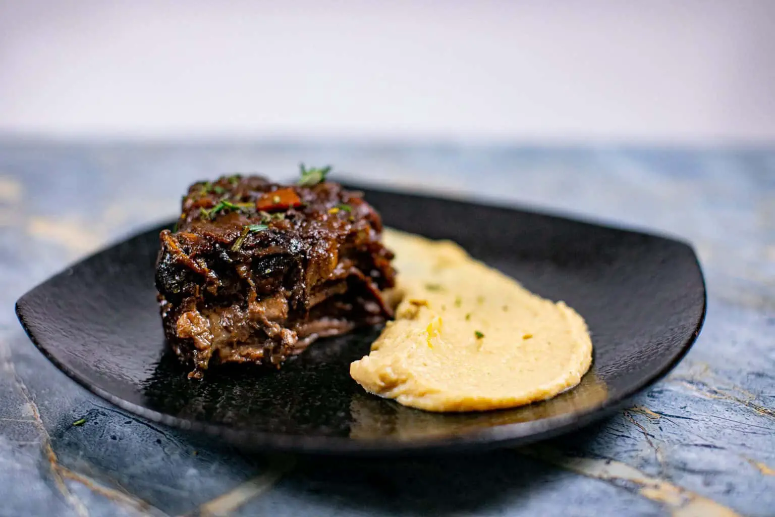 Garlic mashed parsnips with meat garnished with herbs served on a black plate placed on a blue surface