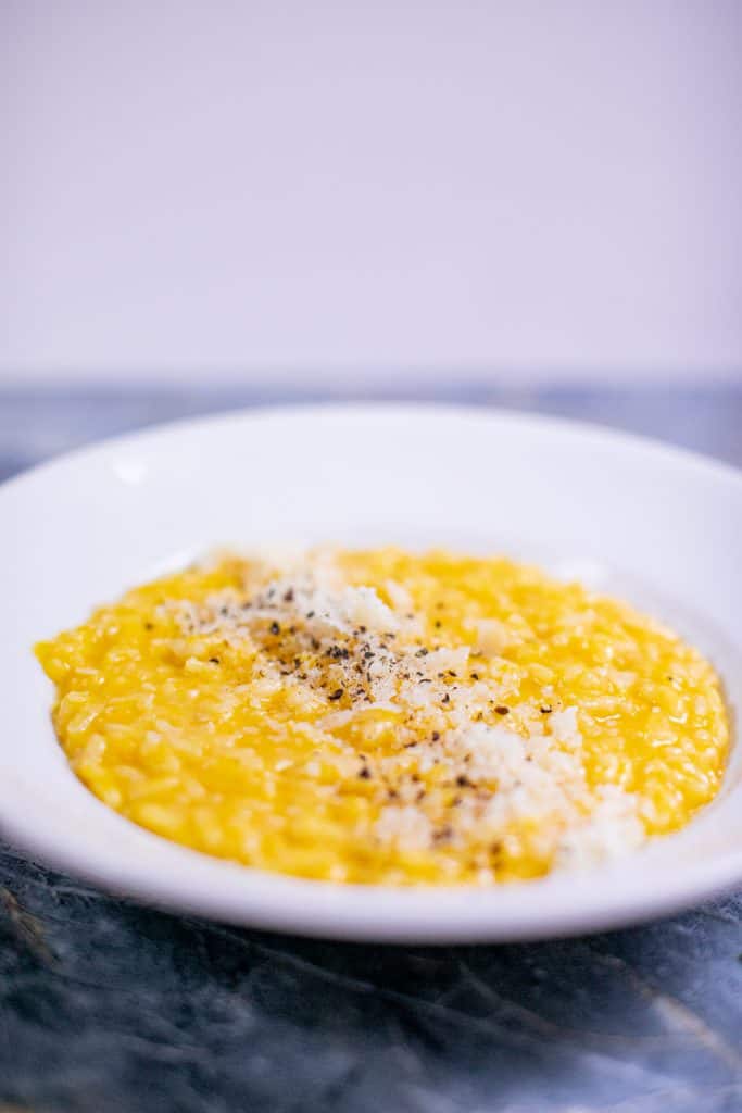 Butternut squash risotto served on a white plate placed on a blue surface