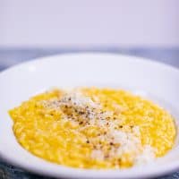 Butternut squash risotto served on a white plate placed on a blue surface