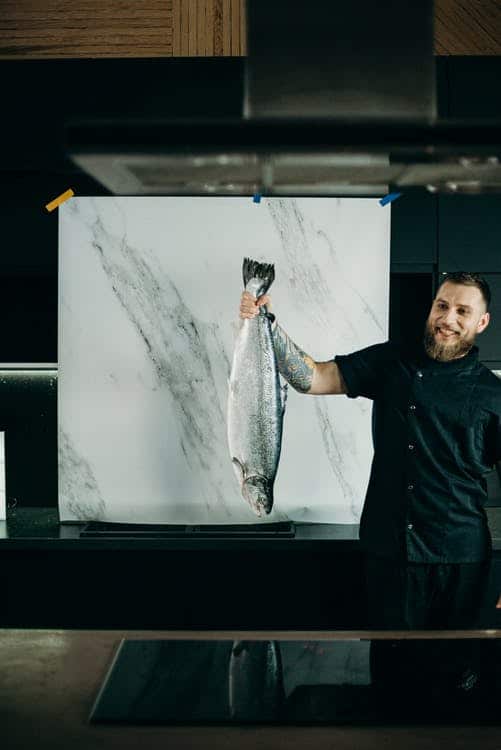 Man holding a large fish and about to demonstrate how to cook and make fish taste good