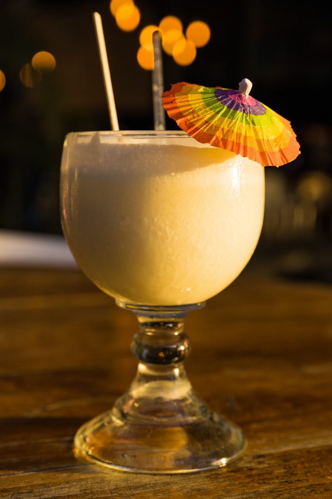 A pina colada in a wine glass with a small umbrella and a straw