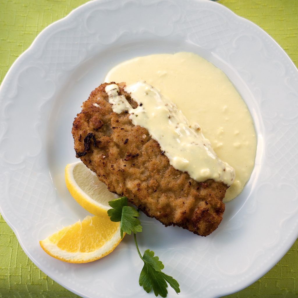 Chicken cordon bleu served on a plate with sliced lemon and white sauce