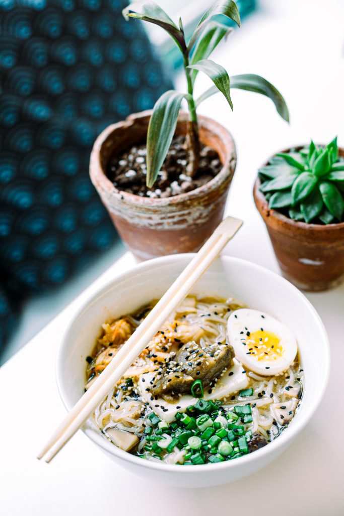 A noodle soup with egg and chopsticks near the plants