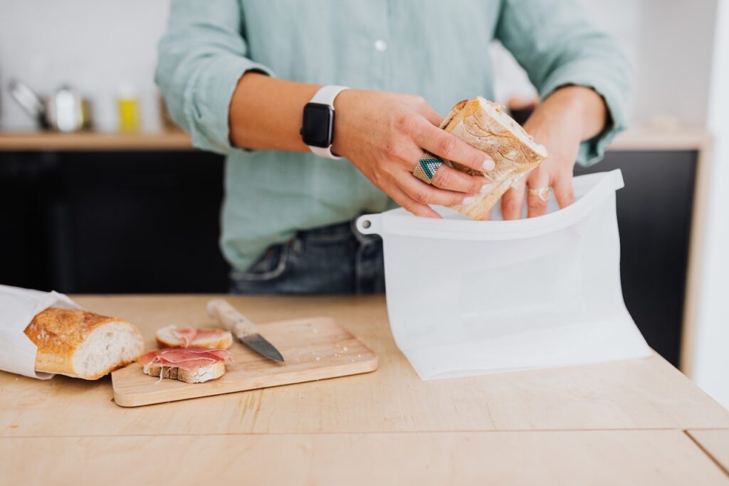 A person in green long sleeves and denim jeans puts bread in a plastic container