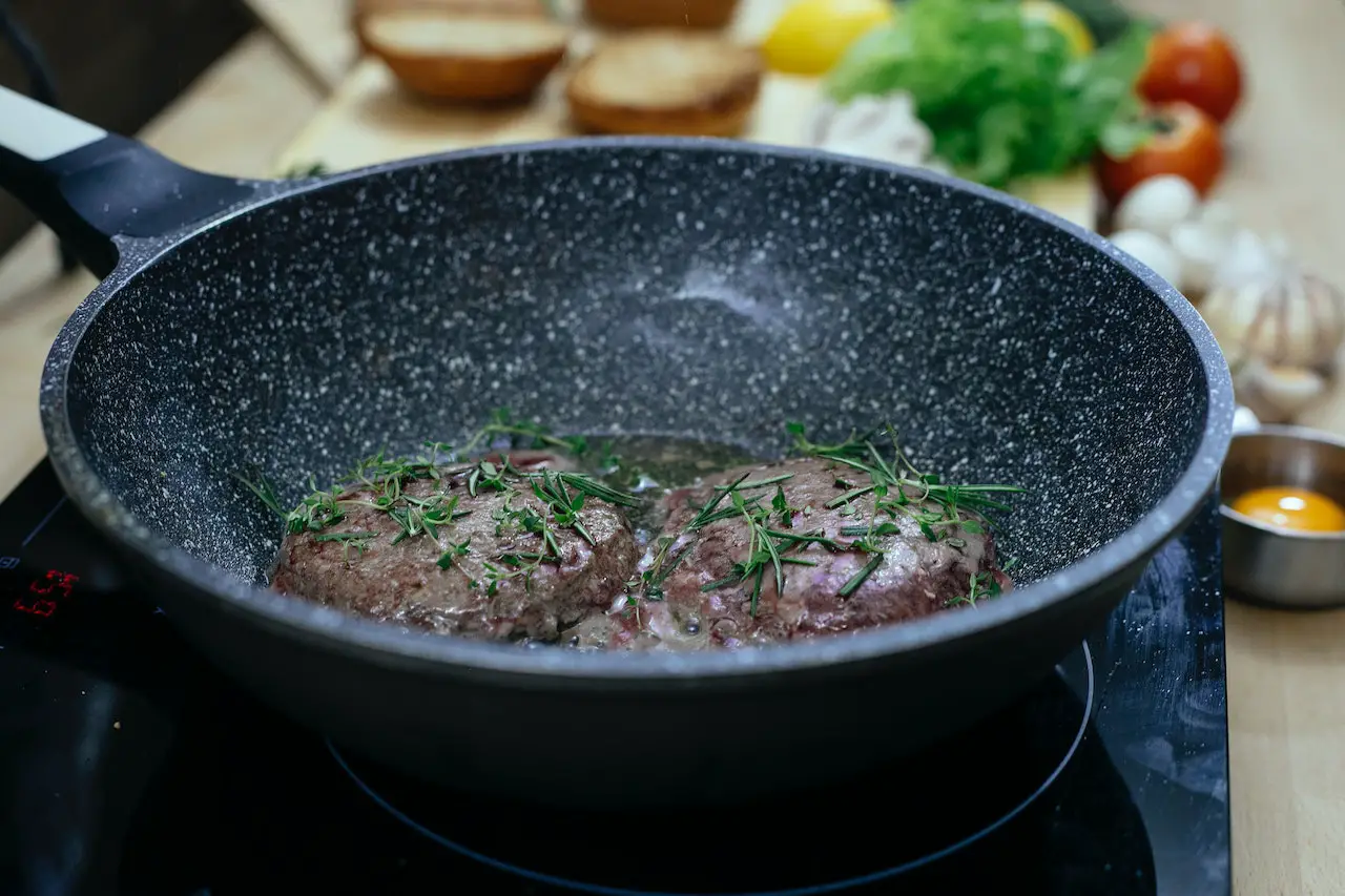 Beef patties garnished with herbs cooked in a black frying pan on an electric stove