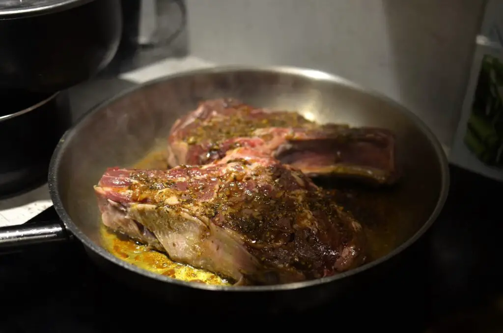 Cooking meat with herbs and spices on a black frying pan
