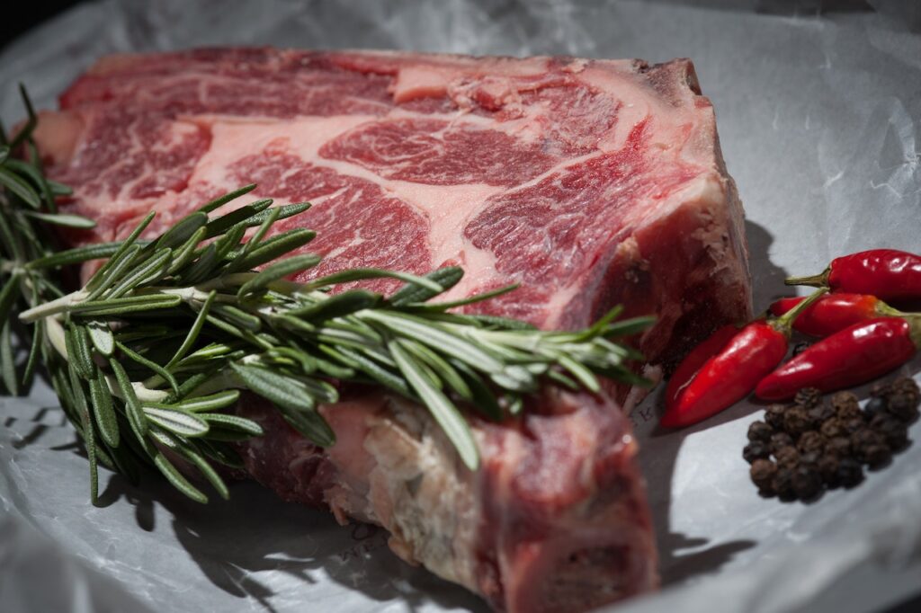 A close-up of red meat with chili pepper and spices on the side on a marble plate