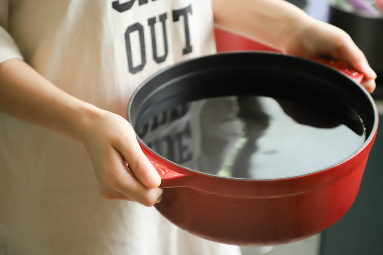 A person holding a red pot filled with water in the kitchen