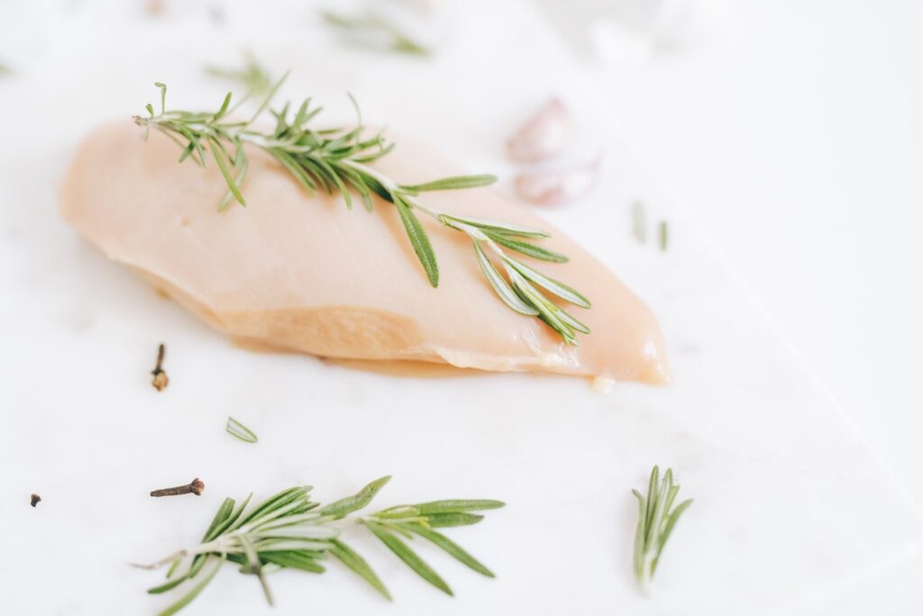 A raw chicken breast with herbs placed on a white ceramic plate