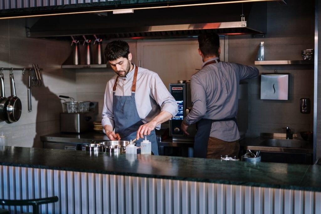 Two men in long sleeves polo and blue aprons preparing dishes in the restaurant