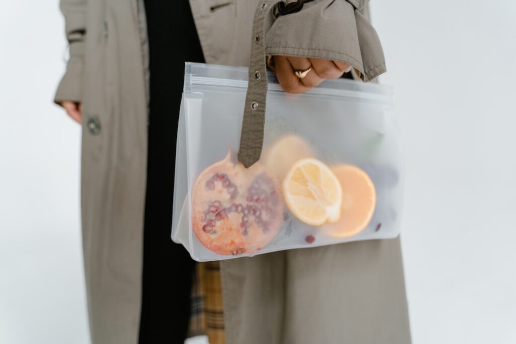 A person in a gray coat holding a zip-lock bag with fruits inside