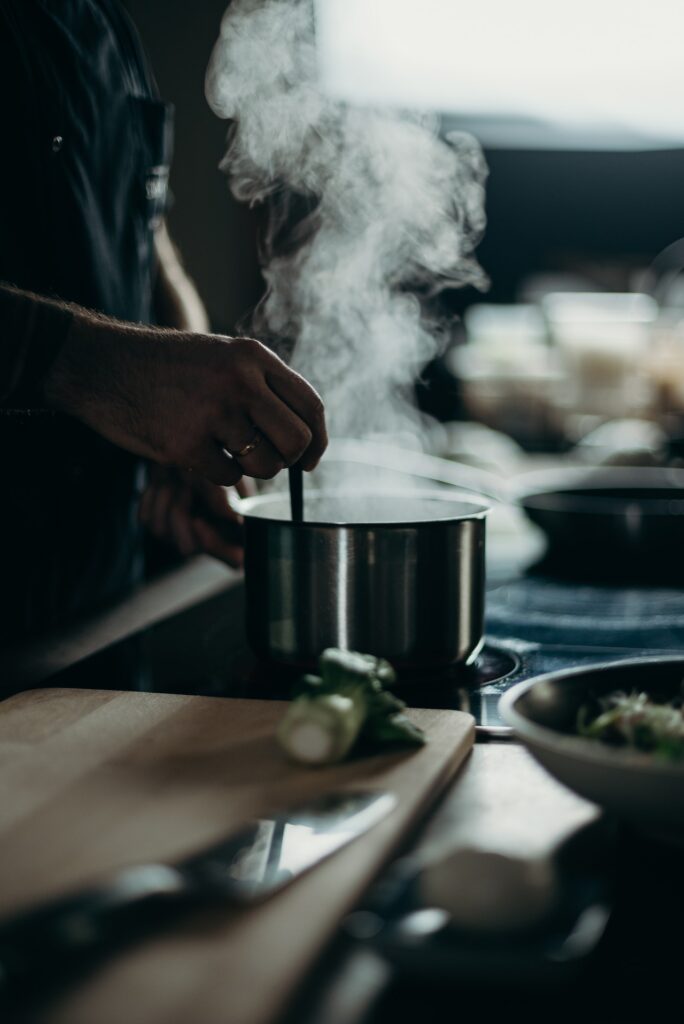 A person using a silver stainless pot and a spoon for cooking on an electric stove